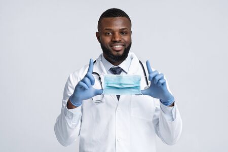 Use face mask during quarantine. Positive african male therapist wearing face mask over white...