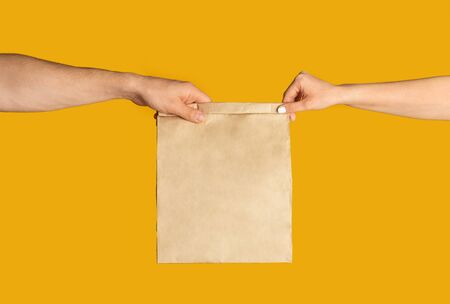 Takeaway food concept. Delivery man giving paper bag with empty space for design to client, orange backgroundの写真素材