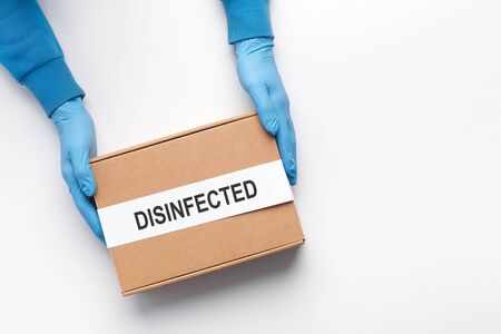 Delivery man holding cardboard disinfected box in medical rubber gloves. Quarantine. Coronavirus....