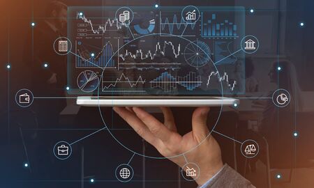 Modern technologies in economics. Hand holds tablet with futuristic virtual hologram graphs and...