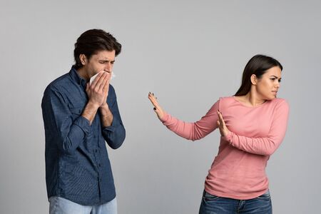 Social Distancing. Young woman disgusted by her sick boyfriend with runny nose, afraid of...