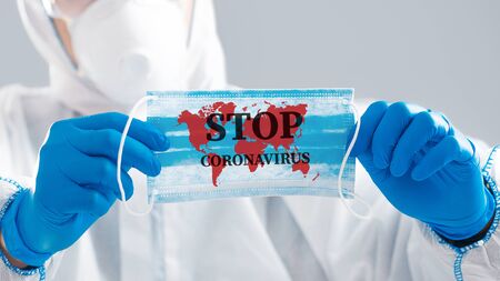 Man in protective suit holds medicine mask with world map and inscription stop coronavirus, close upの写真素材