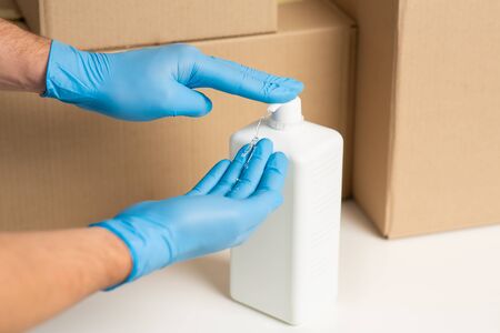 Deliveryman disinfects hands with antiseptic. Cardboard boxes at backgroundの写真素材