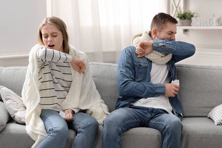 Right way to cough. Young man and woman coughing into their elbows at homeの写真素材