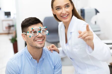 Eye Test Concept. Beautiful female optometrist checking patients vision with trial frame, pointing at chartの写真素材