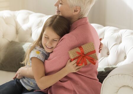 Thankful girl with gift box hugging her grandmother at home