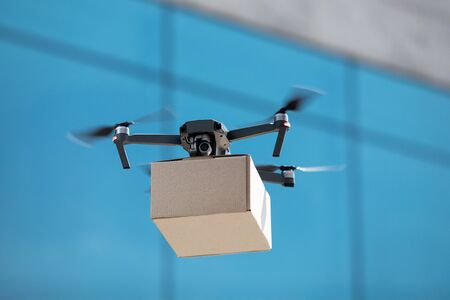 Drone for air delivery. Cardboard package shipment by helicopter drone through the city while quarantineの写真素材