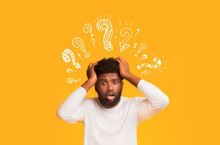 What is going on. Shocked black guy with question mark over his head pulling his hair over orange backgroundの写真素材