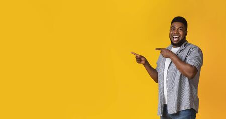Great offer. Joyful black guy pointing aside at copy space on yellow studio background with two hands, panoramaの写真素材