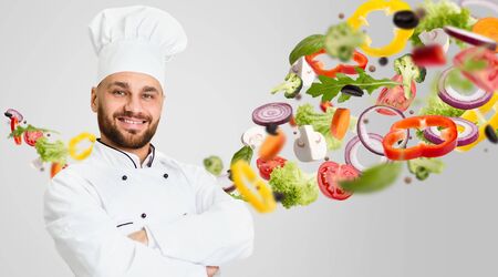 Healthy recipes concept. Happy cook wearing white uniform and vegetables in air on grey background. Collage with blank space. Panoramaの写真素材