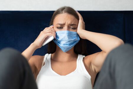 Coronavirus Self-Isolation. Unhappy Girl Talking On Cellphone Sitting On Couch At Home During...