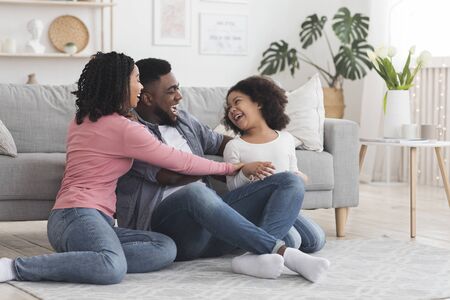 Cheerful black family having fun at home, parents tickling their daughter, laughing together, spending quarantine time in isolation, free spaceの写真素材
