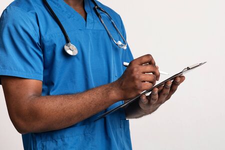 Cropped of black physician with stethoscope filling medical form, white background, copy spaceの写真素材