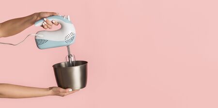 Closeup of young woman holding electric mixer and bowl on pink background, copy space. Panoramaの写真素材