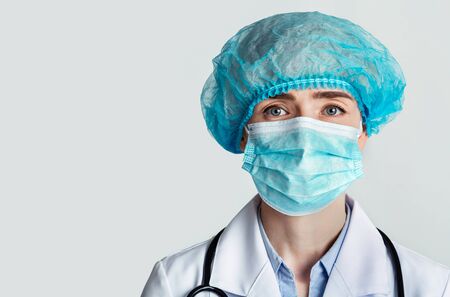 Therapist in a protective mask and hat and stethoscope on light backgroundの写真素材