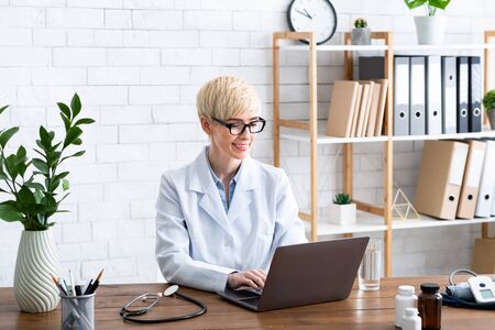 Therapist in workplace. Pretty woman doctor in office at table with laptopの写真素材