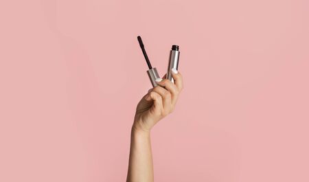 Beauty and makeup concept. Young girl holding mascara on pink background, close upの写真素材