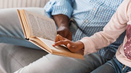 Stay home activities. Lillte African American girl reading fairy tale with her granddad, closeup of...