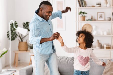 Stay home, have fun. African American granddad dancing with his little granddaughter in light roomの写真素材