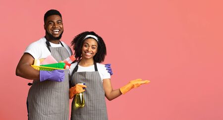 Team of professional cleaners posing with sanitary supplies in hands and pointing aside at copy space over pink background, panoramaの写真素材