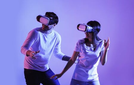 Millennial guy and girl in virtual reality glasses in neon