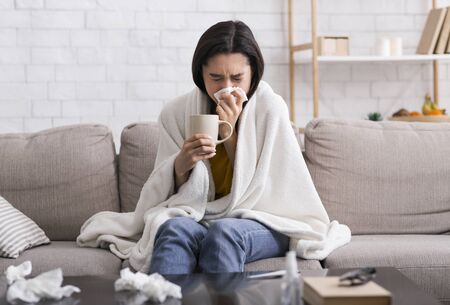 Viral infection outbreak. Millennial woman with bad cold drinking hot tea at homeの写真素材