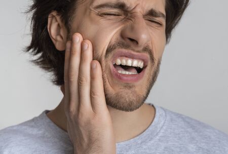 Young male feeling tooth pain, holding cheek with hand