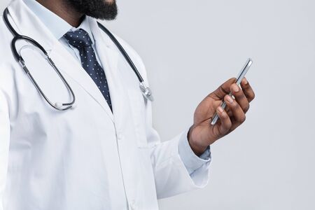 Text your doctor during quarantine. Cropped of african american doctor using smartphone over white studio backgroundの写真素材