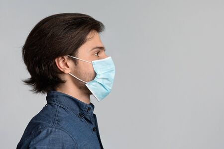 Profile portrait of millennial man wearing protective medical face mask and looking at copy space over light backgroundの写真素材