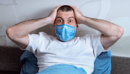 Coronavirus Panic And Anxiety. Scared Man Holding Head In Hands Looking At Camera In Fear Sitting In Bed At Homeの写真素材