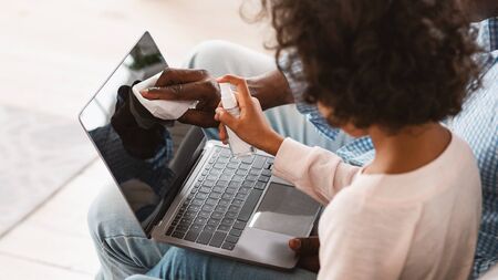Coronavirus hygiene. African American child and her grandpa cleaning laptop with antiseptic, panoramaの写真素材