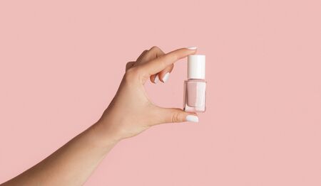 Unrecognizable young girl holding bottle of nail polish on pink background, close up with copy space. Panoramaの写真素材