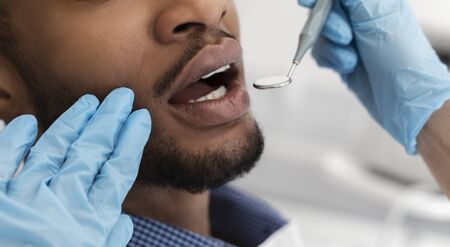 Cropped of dentist hands in gloves checking black man mouth with toolsの写真素材