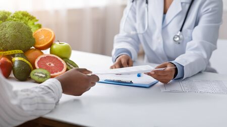 Cropped of black female doctor and patient hands holding document, clinic interior, panoramaの写真素材