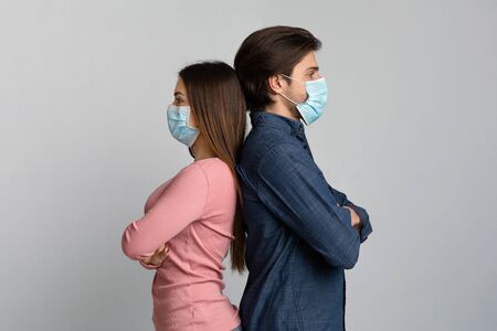 Young woman and man in medical masks standing back to back over light background in studio, copy spaceの写真素材