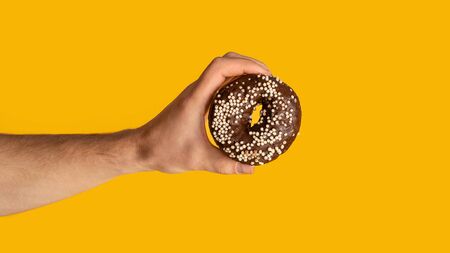 Closeup of male hand showing sweet chocolate donut on orange background, copy space. Panoramaの写真素材