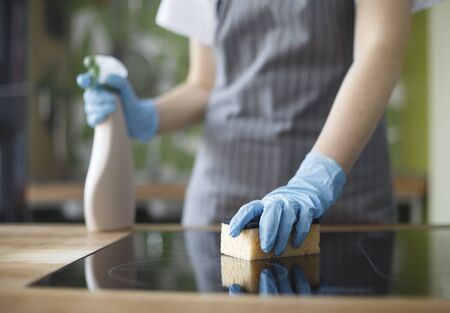 Quarantine cleaning. Unrecognizable woman cleaning kitchen in gloves with disinfecting spray, blurred backgroundの写真素材