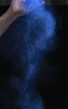 Hand sprinkles blue dry paint forming beautiful cloud on black backgroundの写真素材
