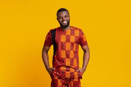 Smiling african guy in authentic clothes posing over yellow studio backgroundの写真素材
