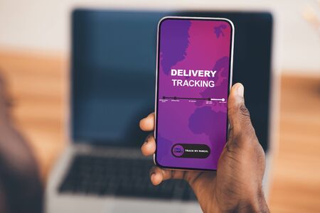 Useful tracking delivery App. Close-up of african man holding mobile phone with app on screen