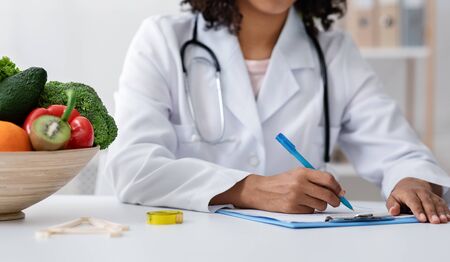 Cropped of african american female doctor dietologist filling medical chart, working at clinicの写真素材