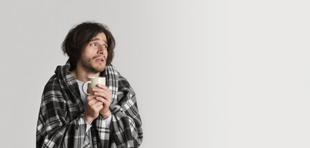 Sick exhausted man in plaid, holds cup of hot drink and looks at empty spaceの写真素材