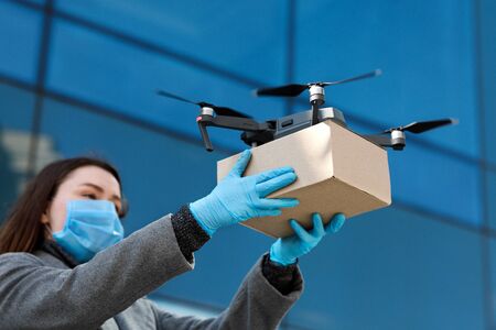 Delivery of the future. Woman in protective mask and gloves receiving cardboard parcel with foodの写真素材