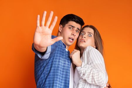 Guy protects frightened girl isolated on orange backgroundの写真素材