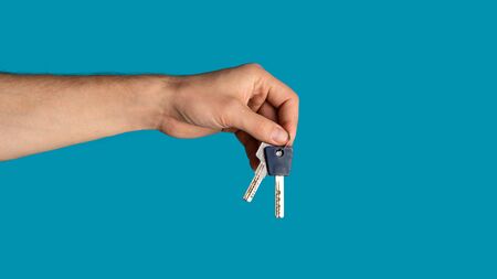 Unrecognizable young guy showing keys to new home on blue background, closeup. Copy space. Panorama