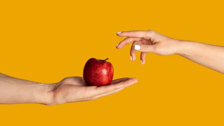 Man and woman with ripe red apple on orange background, close up of hands. Panorama