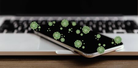 Coronavirus cells on smartphone laying on laptop keyboard. Virus spread by contaminated surface in office, panoramaの写真素材