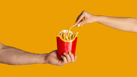 KHARKIV, UKRAINE - APRIL 4, 2020: Close up of guy and girl eating french fries from McDonalds, orange background. Panoramaのeditorial素材