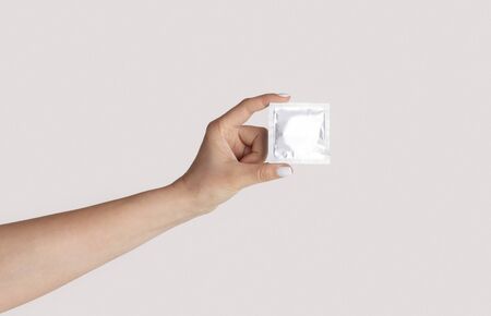 Safe sex. Millennial girl showing condom with wrapper on light background, close up of hand. Panoramaの写真素材