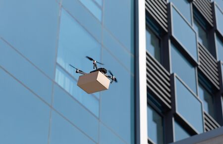 Quadrocopter carrying a parcel and flying in the city delivering packages, copy space